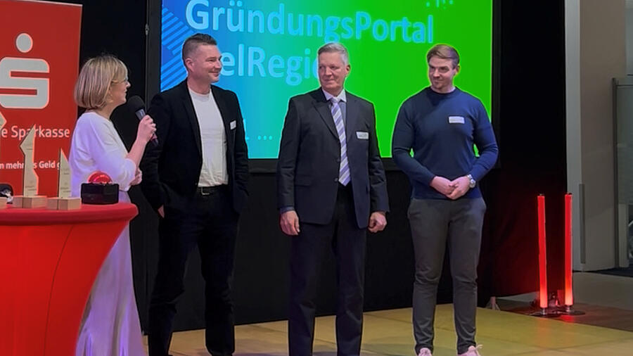Gruppe von Menschen stehen auf einer Bühne vor eine grünen Leinwand