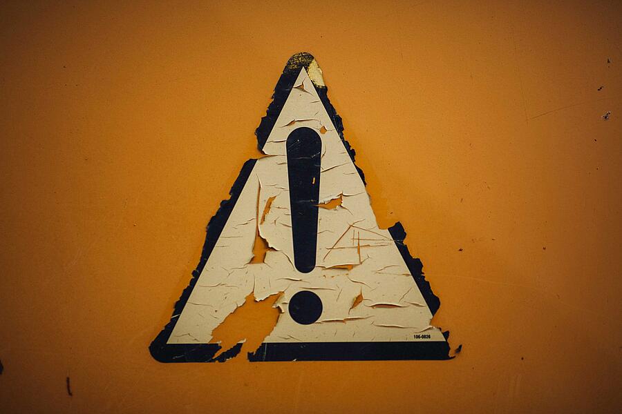 Eine orangefarbene Wand auf der ein Wanddreieck mit Ausrufezeichen klebt.