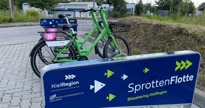 Auf dem Foto ist die Leihfahrradstation der SpottenFlotte zu sehen. Zwei grüne Fahrräder sind hier abgestellt.