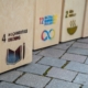 Auf einem gepflasterten Weg sind insgesamt drei Holzwürfel zu sehen, auf denen Nachhaltigkeitsziele der UN gesprüht wurden.