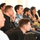 Mehrere Menschen sitzen in einer Veranstaltung in Reihen und hören offensichtlich einem Referenten, einer Referentin zu. Diesen sieht man aber nicht.