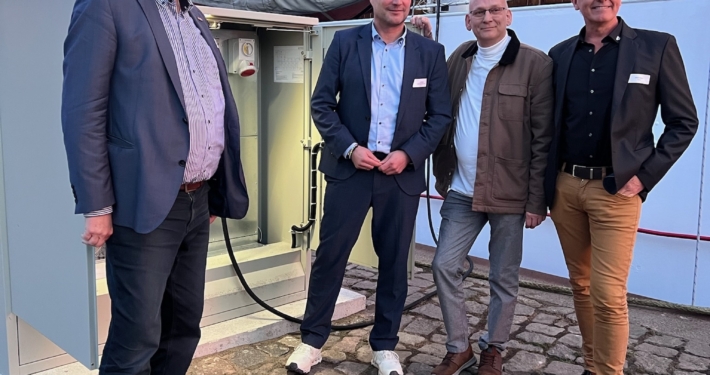 Vier Männer stehen vor einem offenen Stromkasten vor einem historischen Raddampfer.