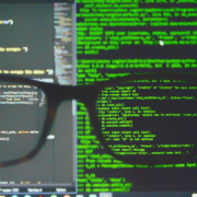 Zu sehen ist ein Quellcode der unscharf ist, im Vordergrund ist eine schwarze Brillle durch die er Quellcode scharf wird.