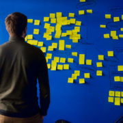 Ein Mann steht vor einer blauen Wand, an der ganz viele gelbe Post-it-Zettel kleben.